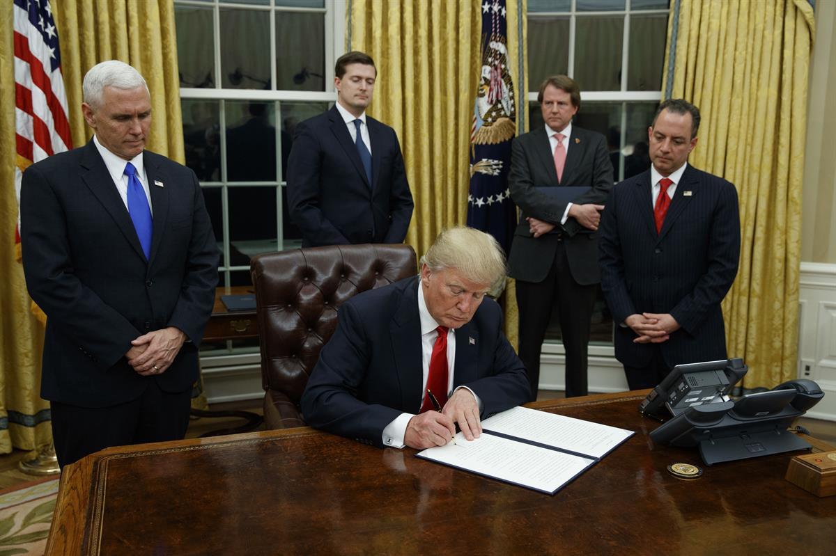 President Donald Trump, flanked by Vice President Mike Pence and Chief of Staff Reince Priebus, signs his first executive order on health care, Friday, Jan 20, 2017, in the Oval Office of the White House in Washington. (AP Photo/Evan Vucci)