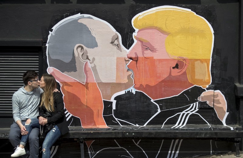 A couple kisses in front of graffiti depicting Russian President Vladimir Putina and President Donald Trump, on the walls of a bar in Lithuania, May 14, 2016. (AP Photo/Mindaugas Kulbis)