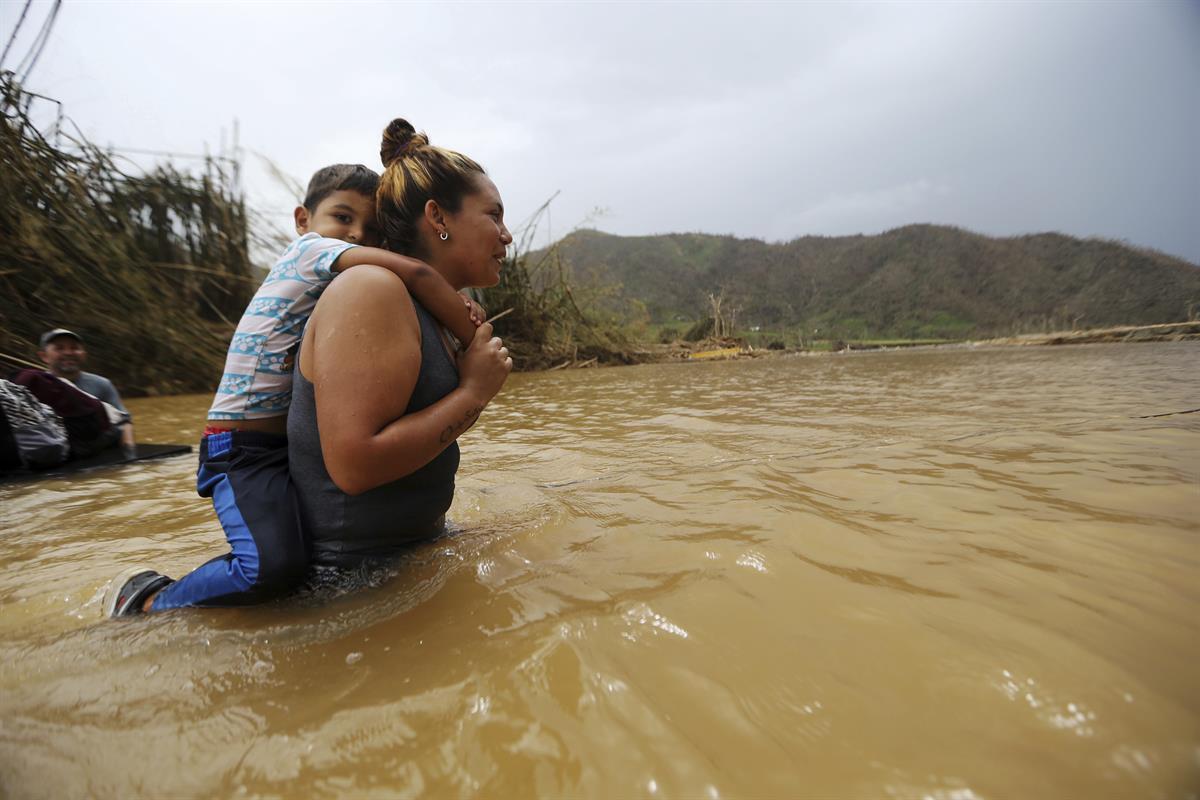 Marlene Ojeda carries her son Esaid Marrero through the Rio San Lorenzo de Morovis, after the bridge that crosses the river was swept away by Hurricane Maria, in Morovis, Puerto Rico, Wednesday, Sept. 27, 2017 (AP Photo/Gerald Herbert)