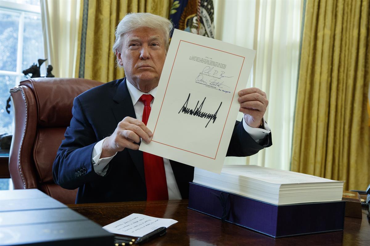 President Donald Trump shows off the tax bill after signing it in the Oval Office of the White House, Friday, Dec. 22, 2017, in Washington (AP Photo/Evan Vucci)