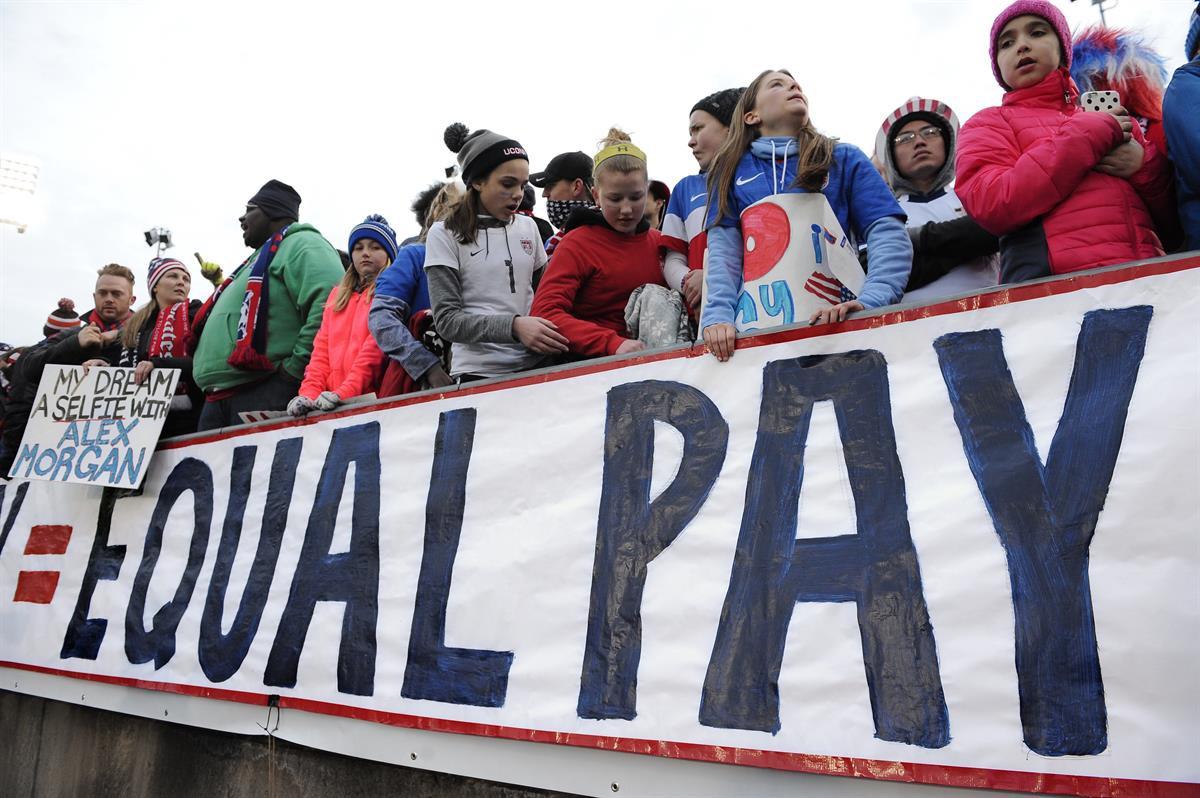Fans stand behind a large sign for equal pay for the women’s soccer team during an international friendly soccer match between the United States and Colombia at Pratt & Whitney Stadium at Rentschler Field in East Hartford, Conn. — April 6, 2016 (AP Photo/Jessica Hill, File)